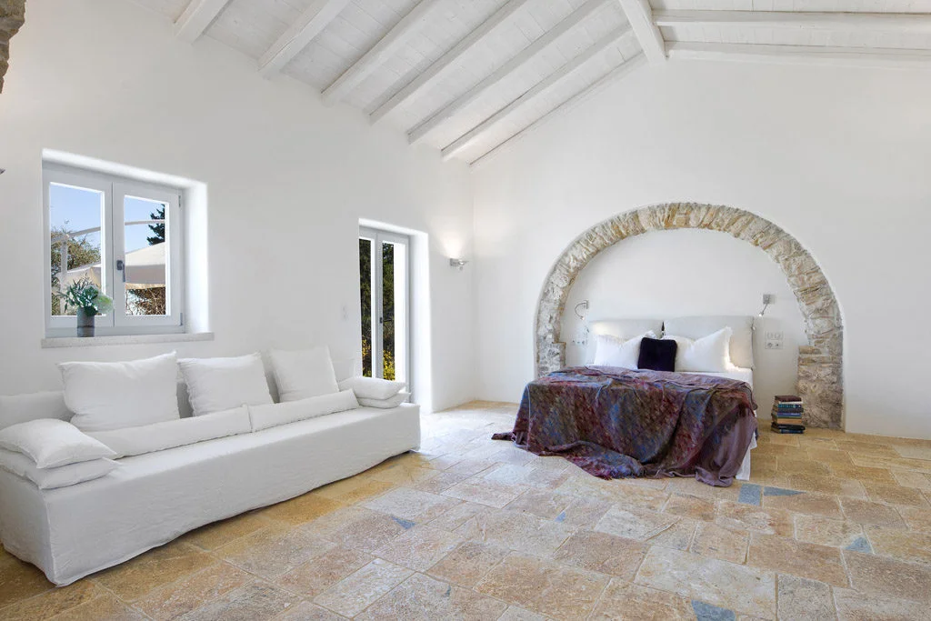 Bedroom with stone arch in wall over bed with white walls and stone flooring
