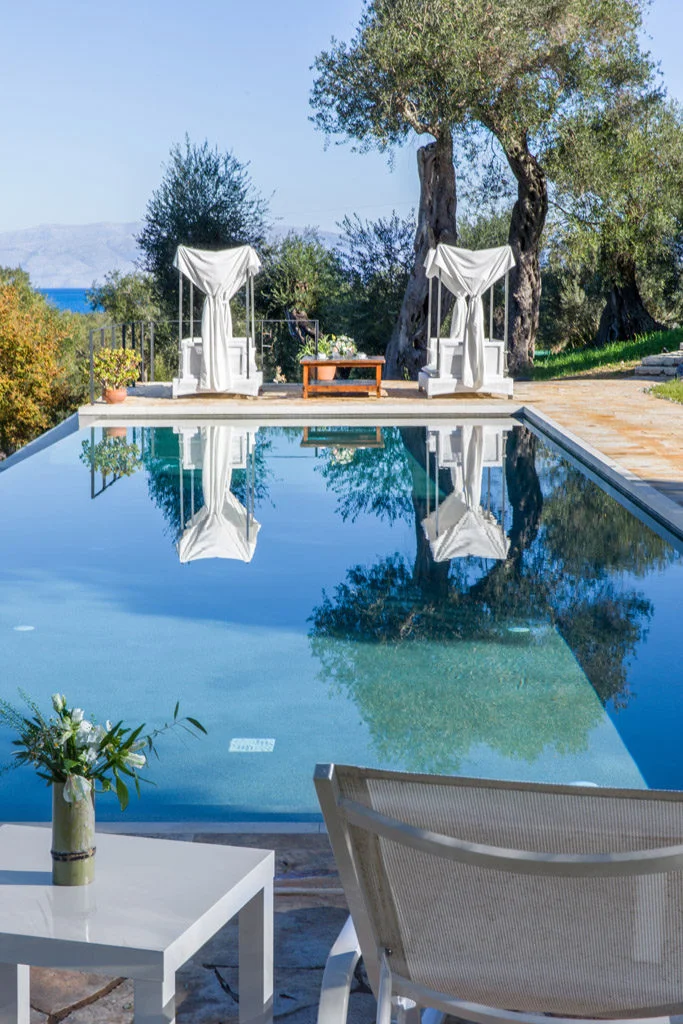 Infinity pool with white patio furniture and olive trees in garden