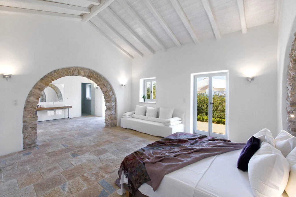 Bedroom with bed and sofa and stone archway leading to bathroom area