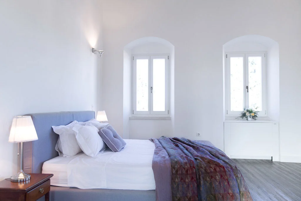 White bedroom with bedside tabe with two windows.