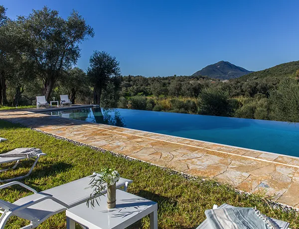 An outdoor infinity pool on a sunny day in Corfu with mountain views