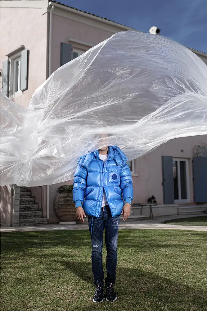 Model wearing blue jacket with plastic sheeting blowing around head.