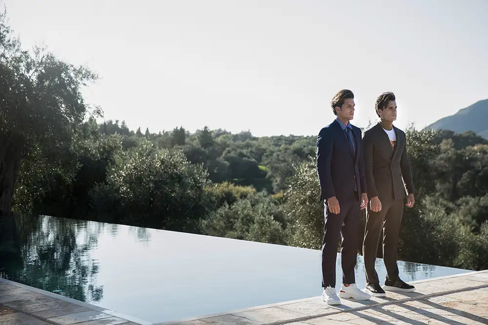 Models wearing suits standing on the edge of the Infinity Pool in the garden of The Courti Estate.