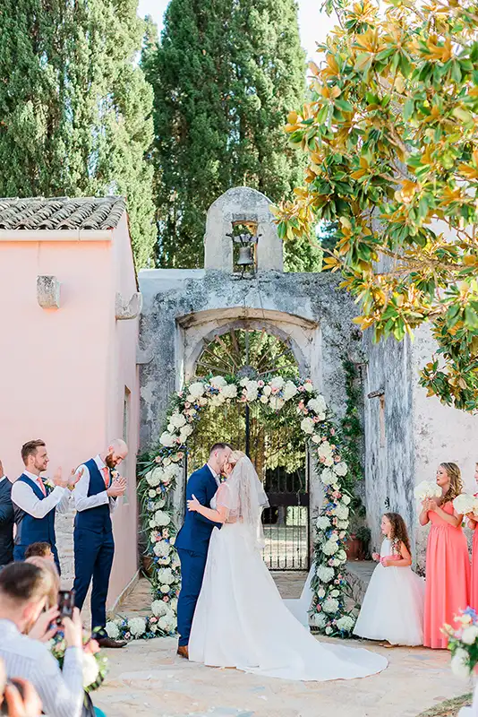 Bride and groom kissing underneath a floral arch in The Courti Estate garden.