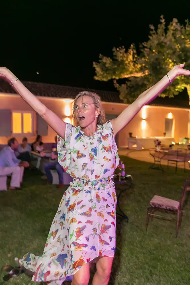 Woman dancing with hands in the air with guests sitting down talking in the background.