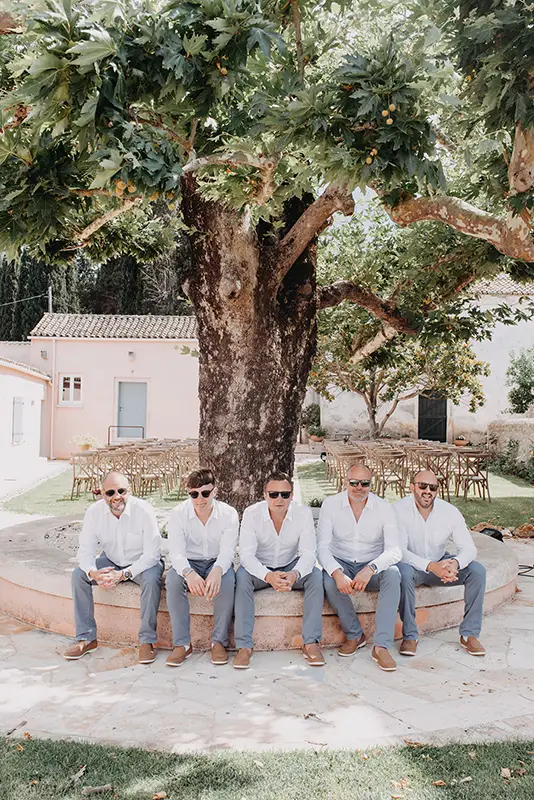 Groom and others sitting down on small wall with olive tree in background