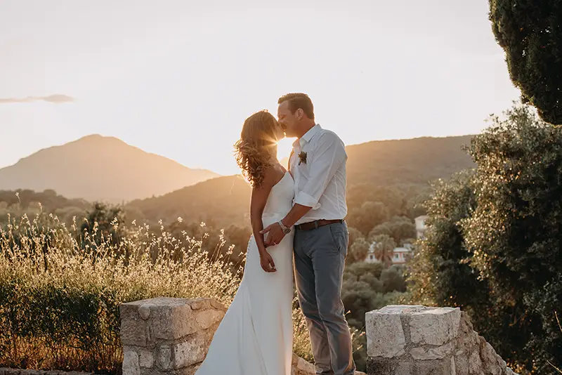 Bride and groom kissing as the sun sets behind a mountain