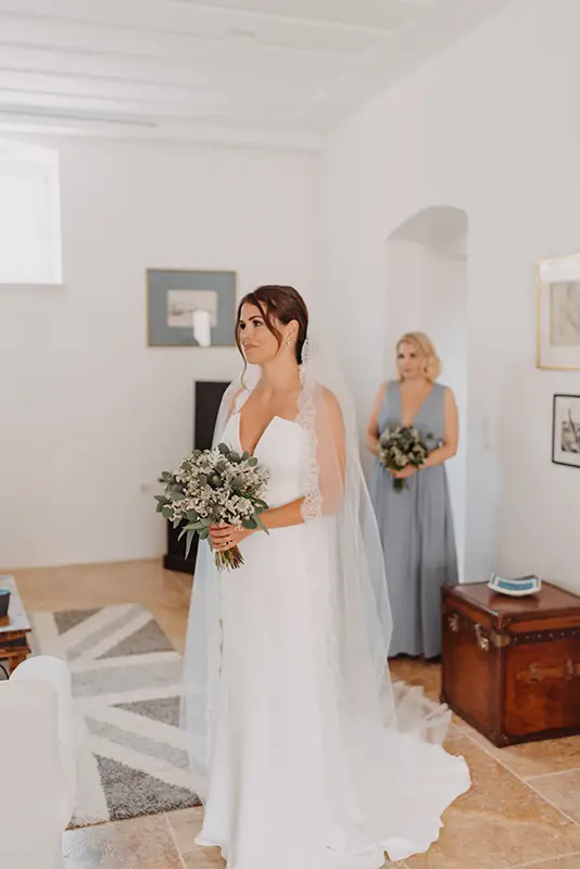 Bride in room with wedding dress and bouquet of flowers