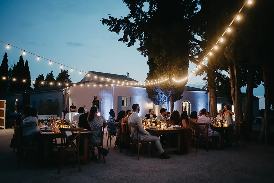 Evening wedding reception with guests seated underneath string lights
