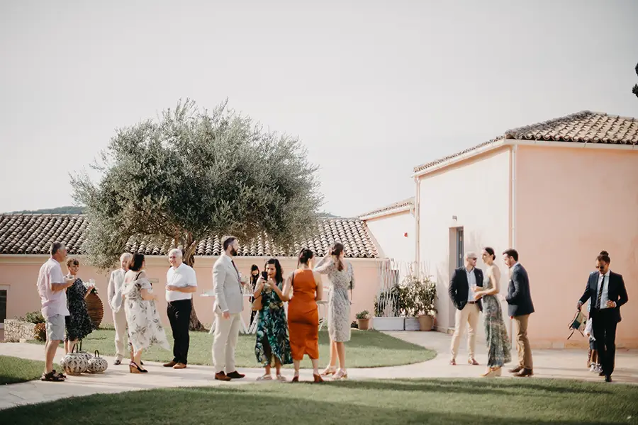 Guests talking in the garden surrounded by buildings with pink walls and a olive tree in the garden