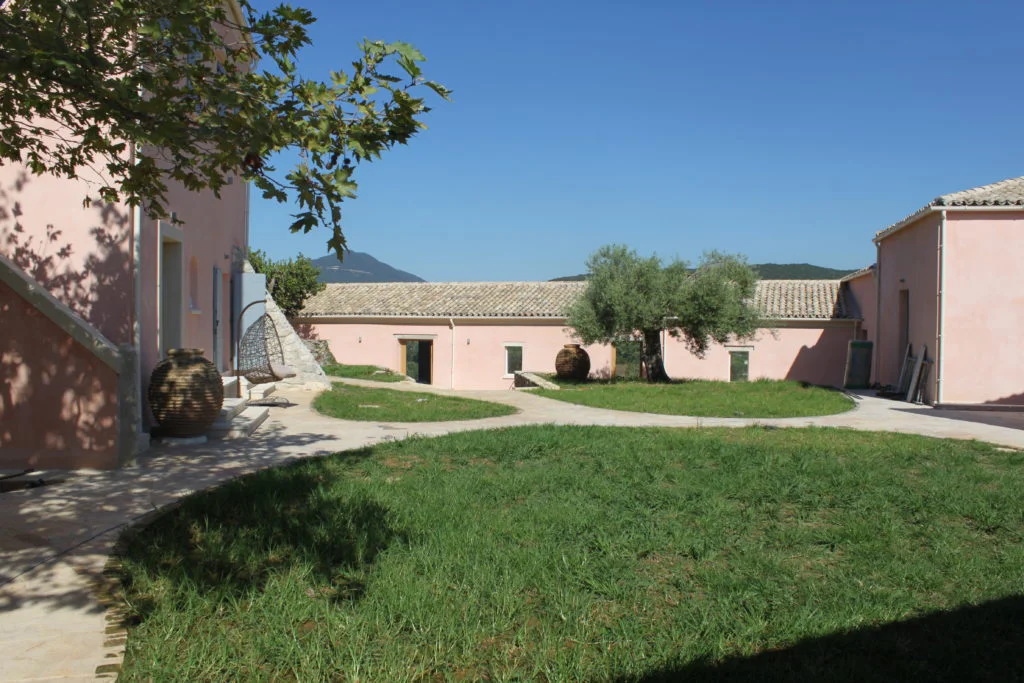 Pink buildings at The Courti Estate with olive tree on lawn