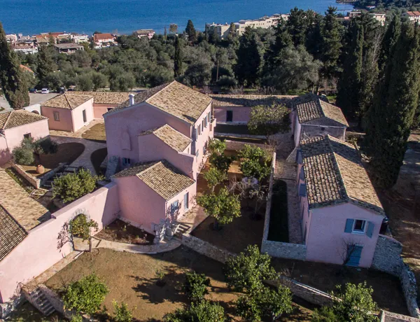 Aerial view of The Courti Estate, a hilltop villa set in a large green open space with the sea in the background.