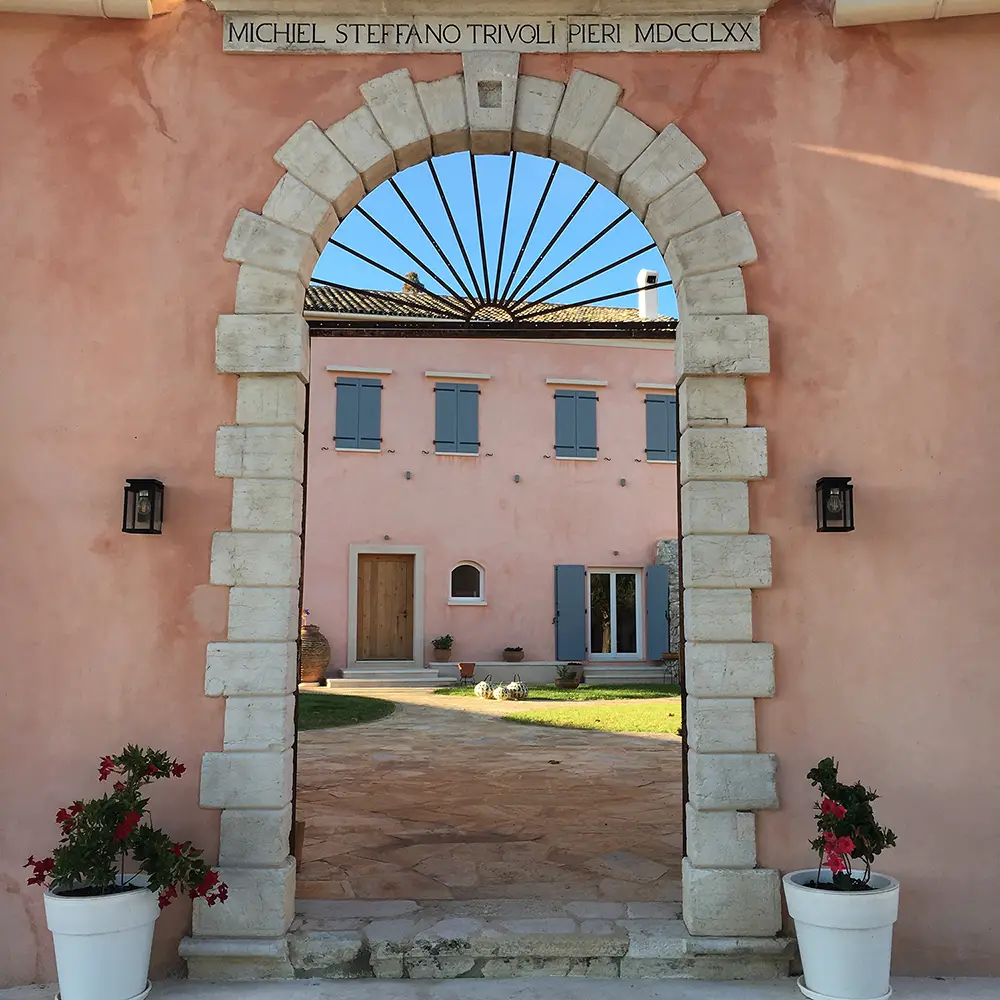 Archway leading into the Courti Estate with pink villas and courtyard.