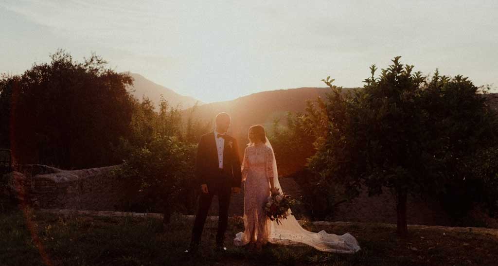 Bride and groom holding hands with mountain scenery and sunset behind.